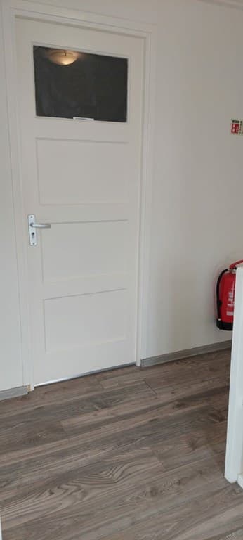 Interieur van een woning met een lichte deur, laminaatvloer en een brandblusser in de hoek.