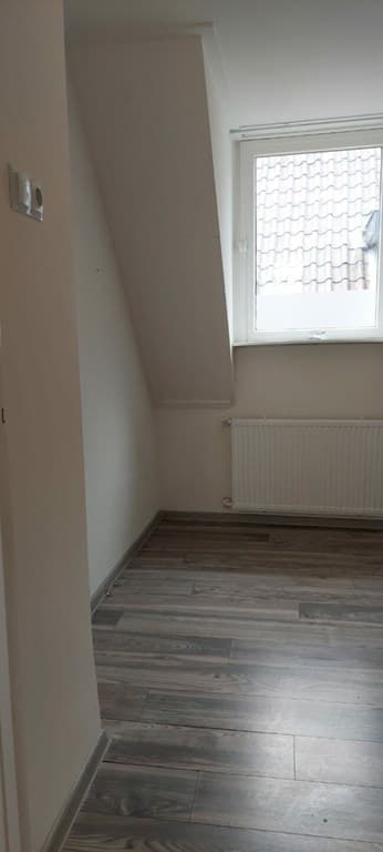 Kamer met schuin plafond, een raam met uitzicht op dakpannen en een radiator aan de wand