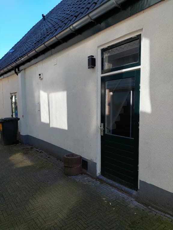 Zijaanzicht van een recreatiewoning met een kunststof deur, trap naar boven en een afvalcontainer naast de gevel