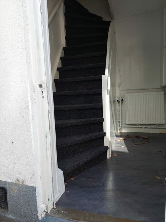 Binnenkant van de woning met een wenteltrap bedekt met zwarte trapbekleding en tegelvloer zichtbaar.