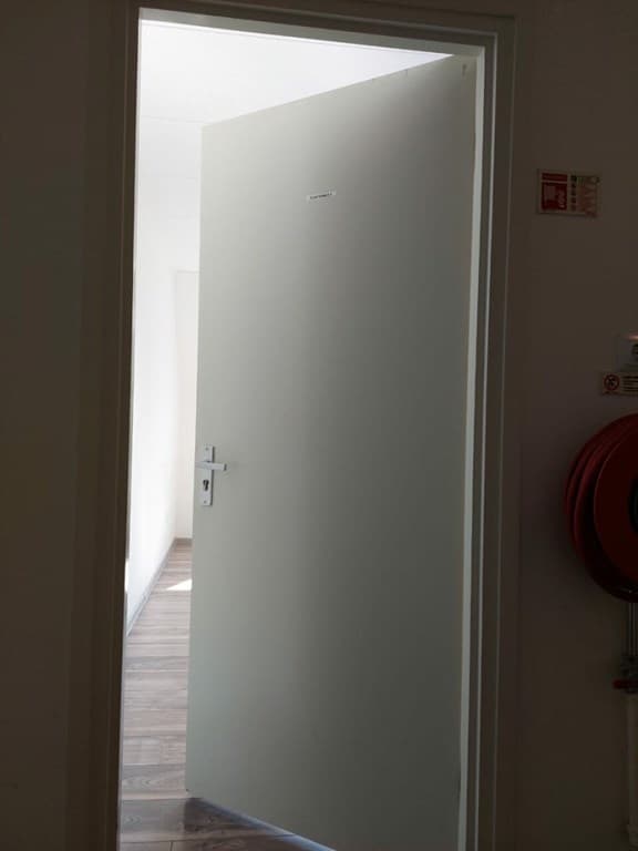 De foto toont een openstaande deur met daarachter een lichte gang en een houten vloer.