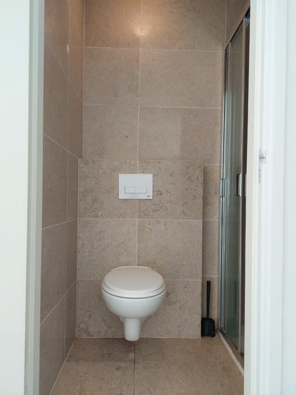 Badkamer met tegelwand, toilet en douchecabine zichtbaar, lichte kleurstelling en moderne uitstraling
