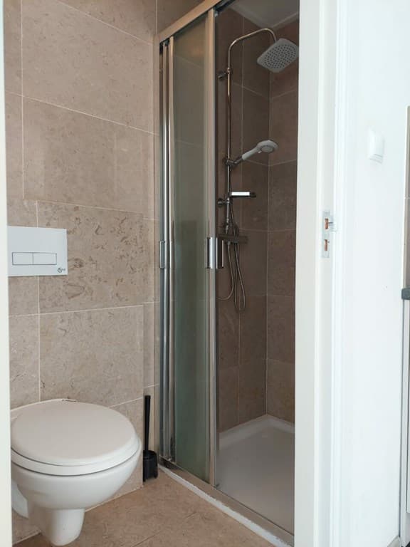 Badkamer met douchecabine en toilet, betegelde wanden en vloer in neutrale kleuren.