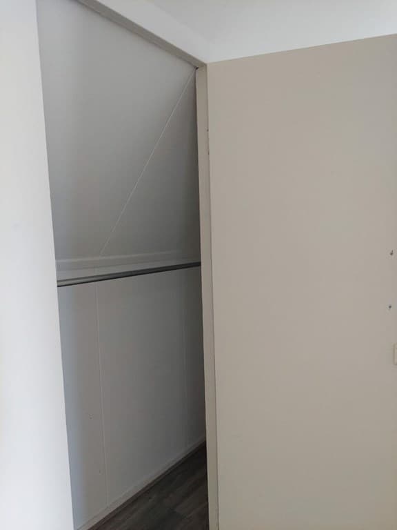 Ingebouwde kast met schuifdeur en schuin plafond in een lichte ruimte.