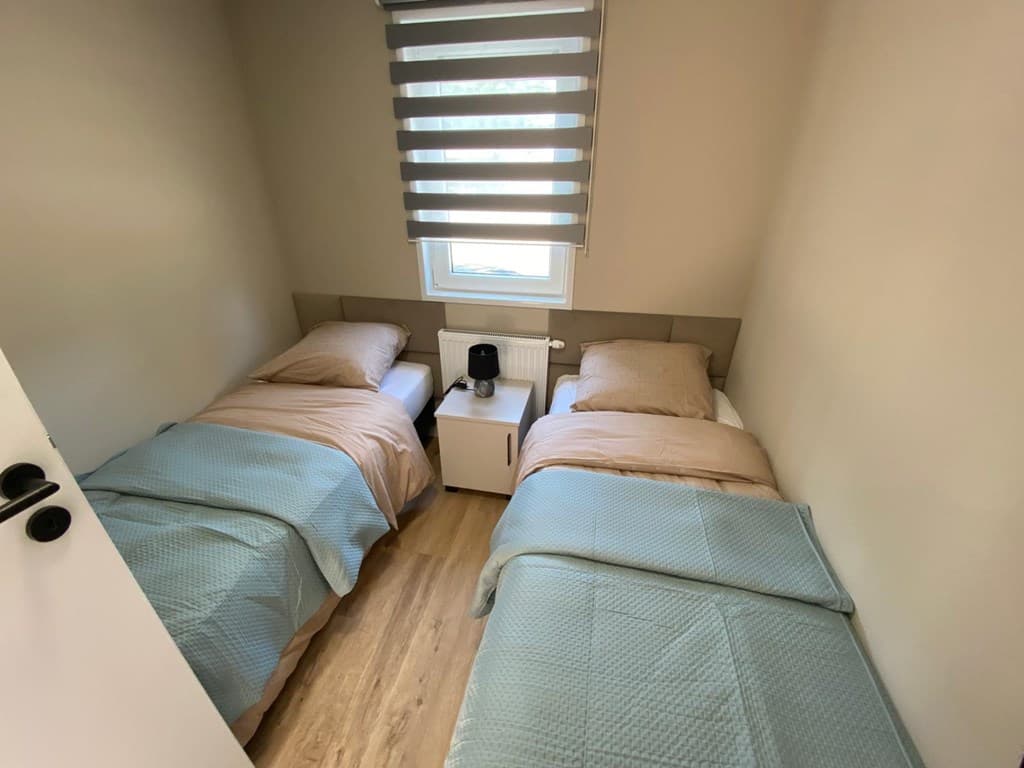 Slaapkamer met twee eenpersoonsbedden, nachtkastje met lamp en een raam met jaloezieën.
