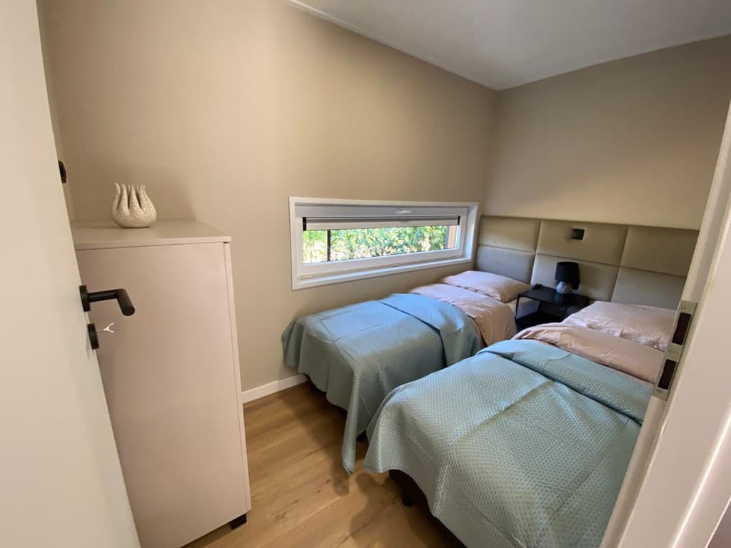 Slaapkamer met twee éénpersoonsbedden, een nachtkastje en een kast naast het raam met uitzicht op de tuin.