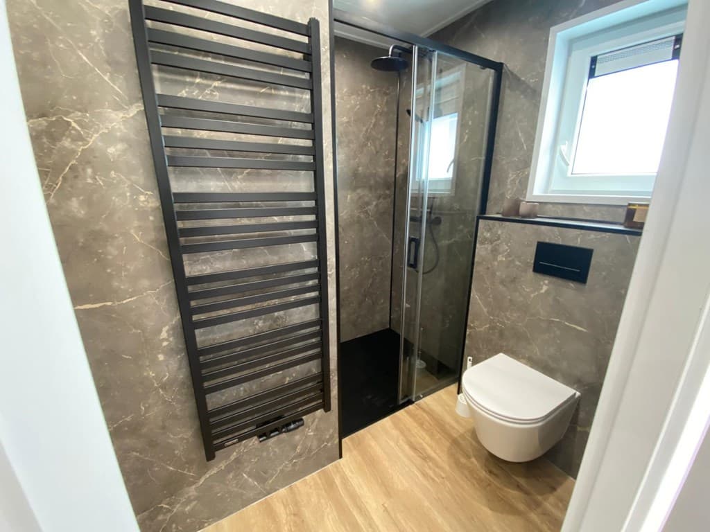 Moderne badkamer met inloopdouche, wandradiator en een toilet, afgewerkt met marmerlook en houten vloer.