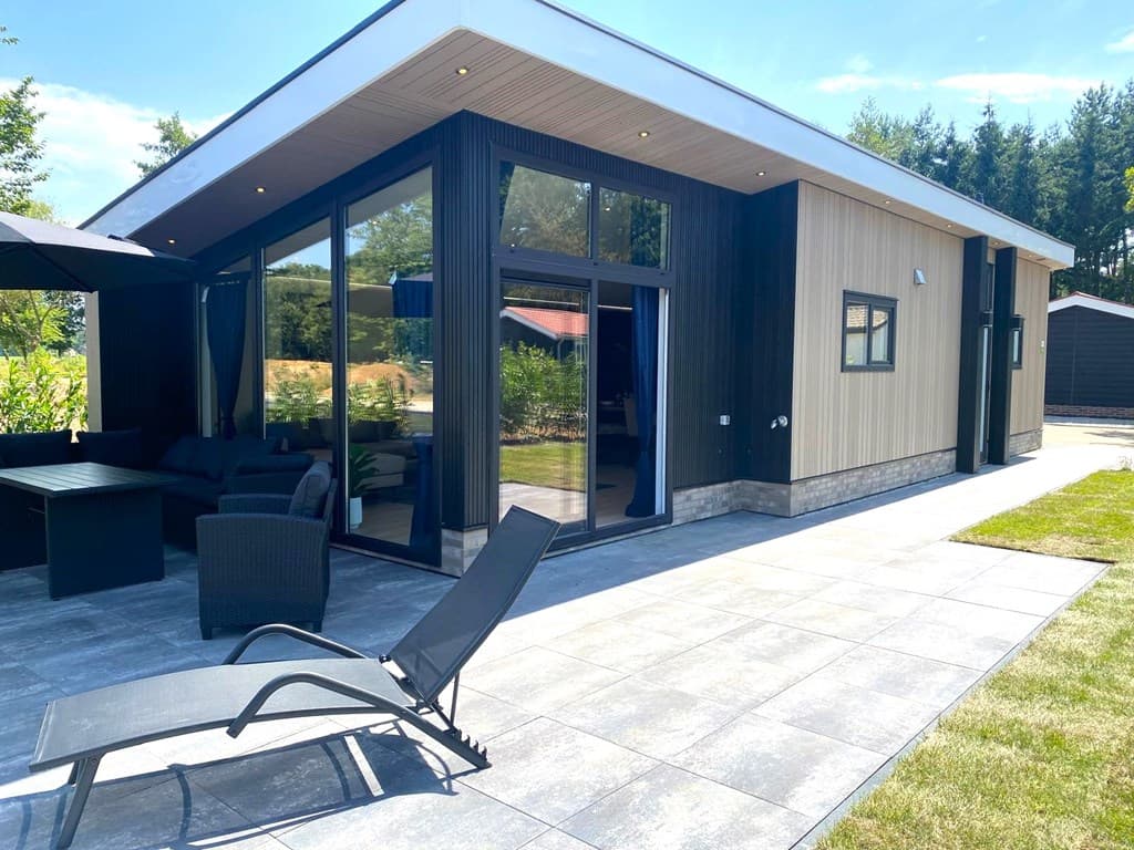 Moderne vakantiewoning met grote ramen, terras en ligstoelen in een groene omgeving in Winterswijk Huppel.