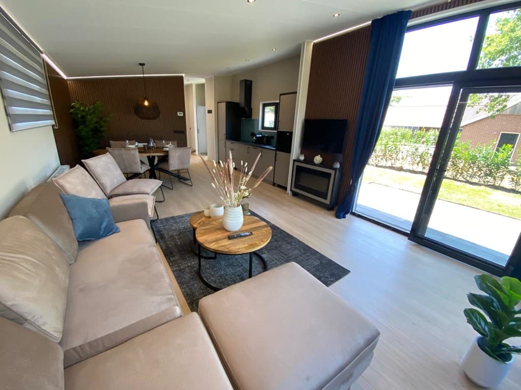 Ruime woonkamer met zithoek, eettafel, moderne inrichting en toegang tot een terras met uitzicht op de tuin.