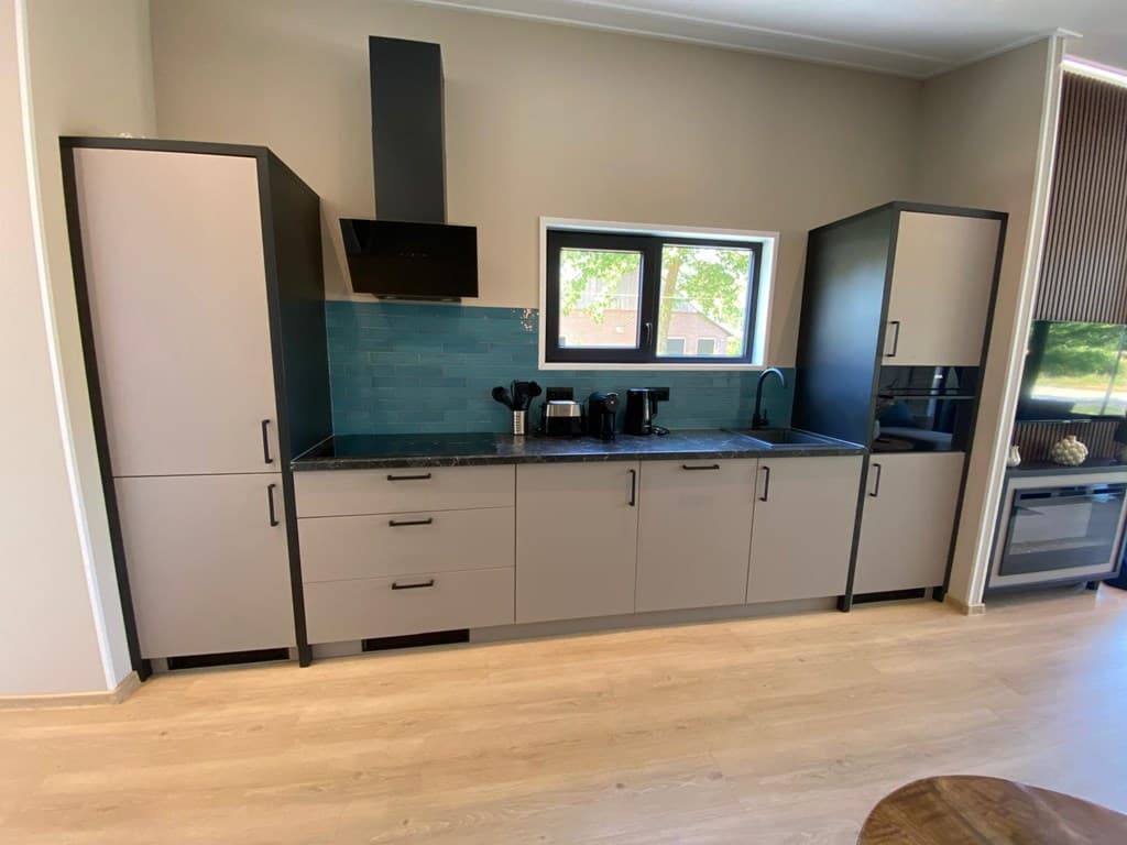 Moderne keuken met lichte kasten, een zwart aanrecht, een afzuigkap en een raam met uitzicht.