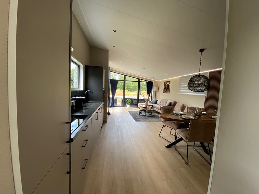 Moderne open keuken met uitzicht op een ruime woonkamer en eetgedeelte met grote ramen en stijlvolle verlichting