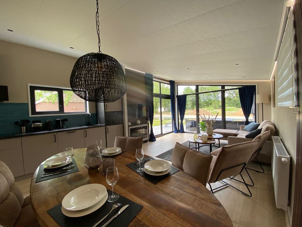 Moderne open woonkamer met eetgedeelte, zithoek en grote ramen, veel natuurlijk lichtinval en uitzicht op de groene buitenrui
