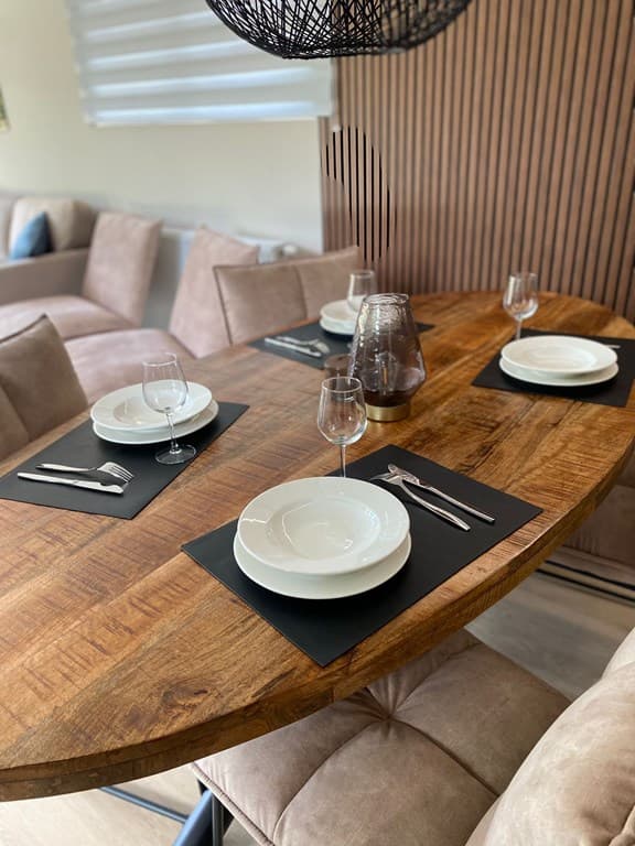 Houten eettafel met borden en glazen in een stijlvolle eetruimte met beige banken op de achtergrond