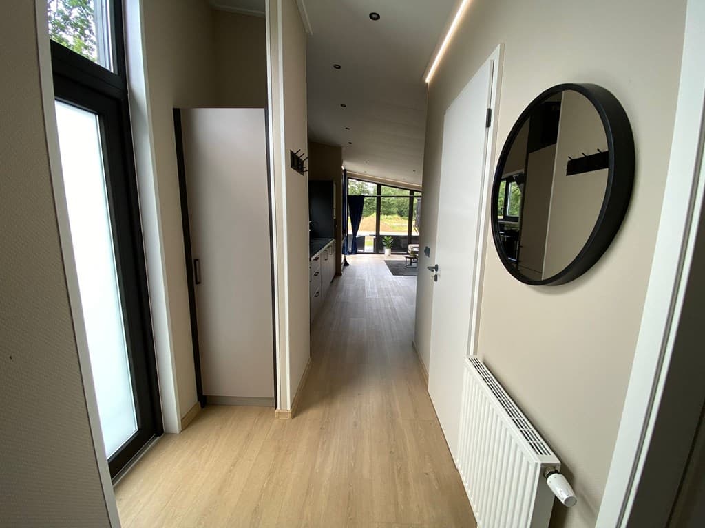Ingang van de woning met een lange gang, meubels en grote ramen die uitkijken op de buitenruimte.