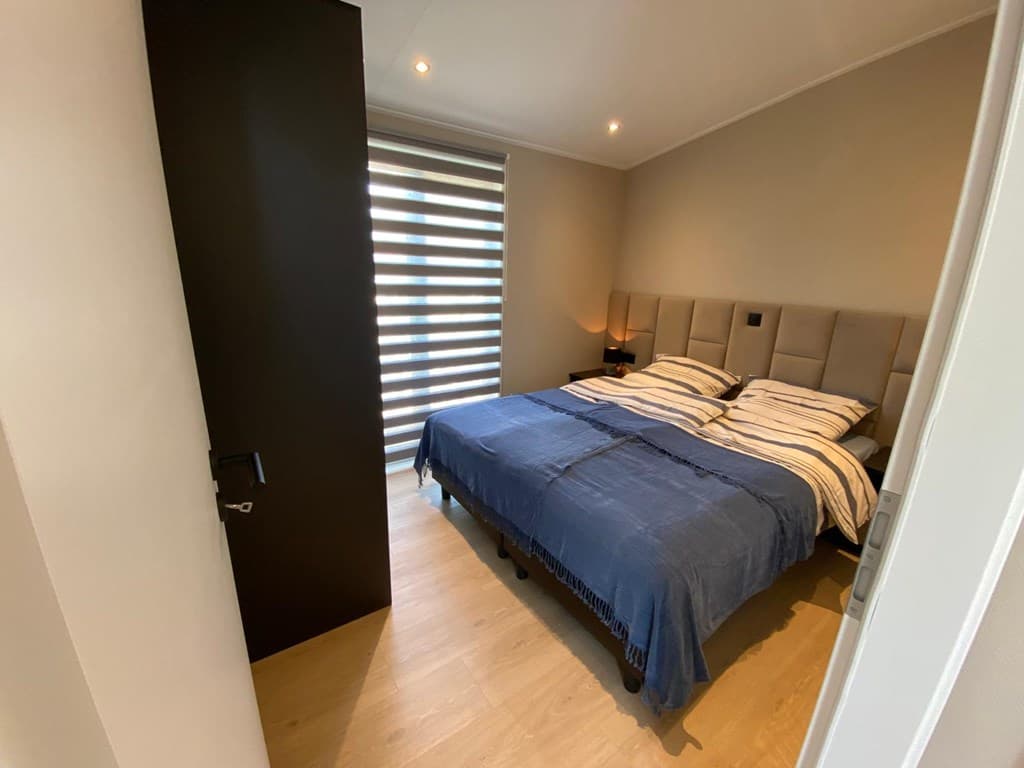 Slaapkamer met een tweepersoonsbed, modern hoofdbord en verduisterende jaloezieën aan het raam
