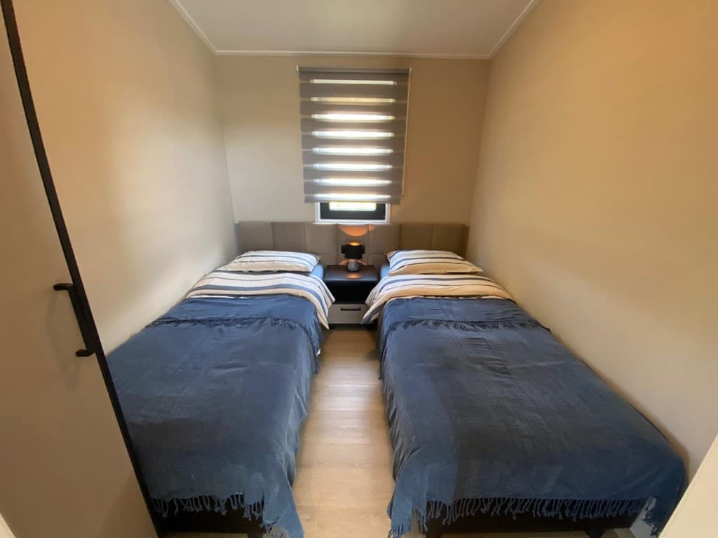 Slaapkamer met twee eenpersoonsbedden, verlichting en een raam met jaloezieën