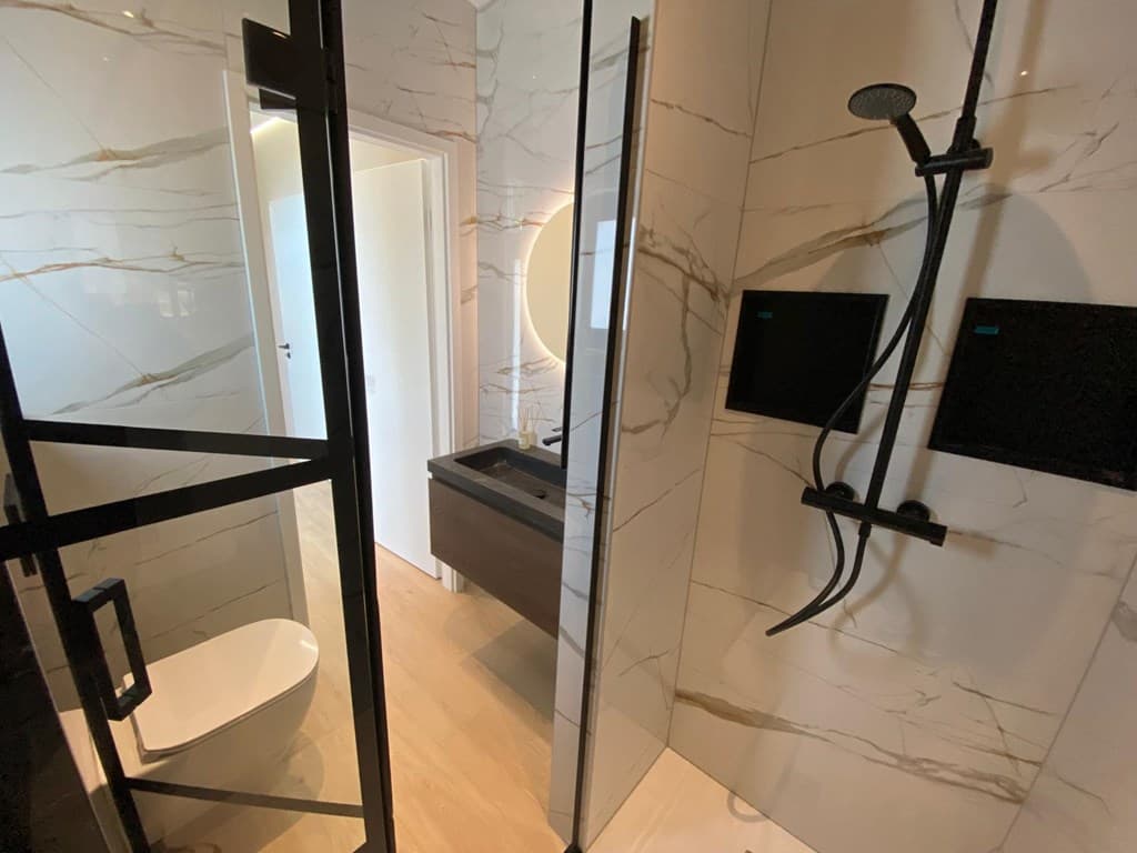 Moderne badkamer met glazen inloopdouche, toilet en wastafel met natuurstenen afwerking en marmerlook wanden