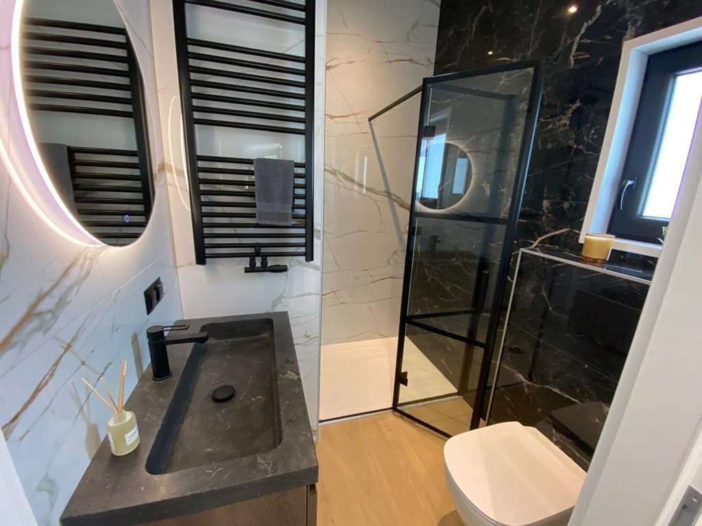 Moderne badkamer met inloopdouche, zwart-witte tegels, ronde spiegel en stijlvolle wastafel met meubel