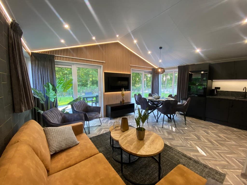 Moderne woonkamer met zithoek, eettafel en grote ramen die uitzicht op de natuur bieden