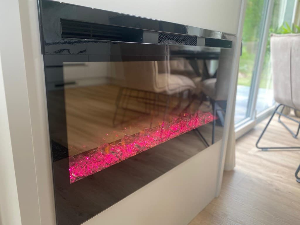 Modern elektrische haard met een glazen voorkant en roze verlichte decoratieve elementen, geplaatst aan een wand.