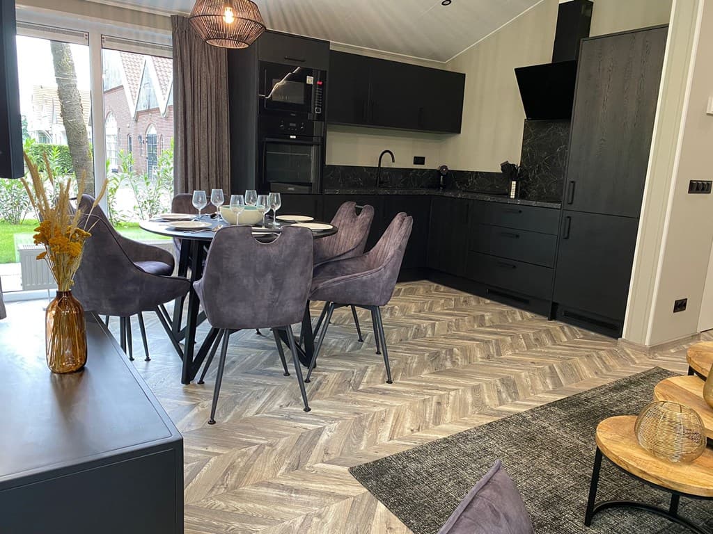 Moderne open keuken met eettafel en stoelen, zwart meubilair en een houten vloer met een visgraatpatroon.