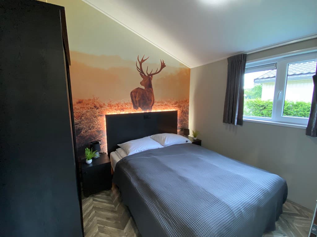 Slaapkamer met tweepersoonsbed, wand met hertentafereel en sfeerverlichting, raam met uitzicht op groen.