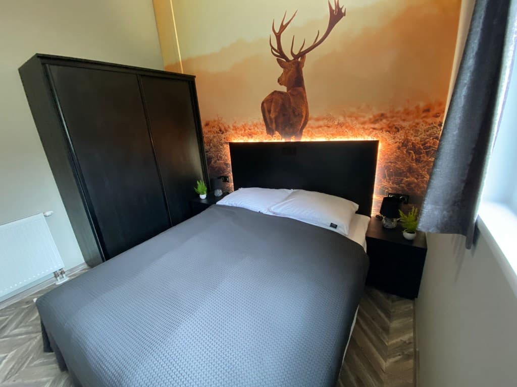 Slaapkamer met een tweepersoonsbed, nachtkastjes, kast en een muurdecoratie van een hert in een natuurlijke omgeving.