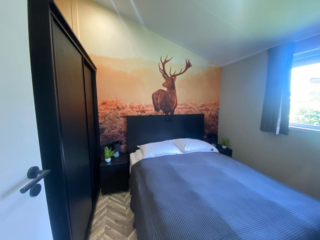 Slaapkamer met tweepersoonsbed en wanddecoratie van een hert, verduisteringsgordijnen en kledingkast.