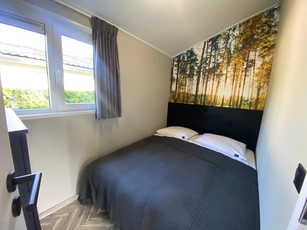 Slaapkamer met een tweepersoonsbed, natuurwanddecoratie en raam met uitzicht op groene begroeiing.