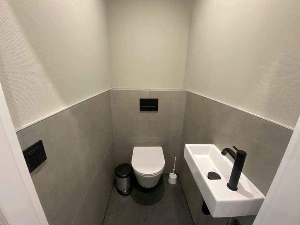 Modern toilet met grijze tegels, wandfonteintje en zwarte armatuur zonder decoratie