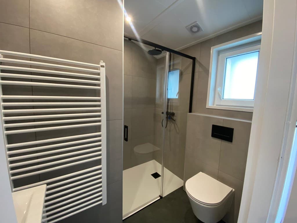Moderne badkamer met inloopdouche, toilet, handdoekenradiator en raampje voor natuurlijk licht