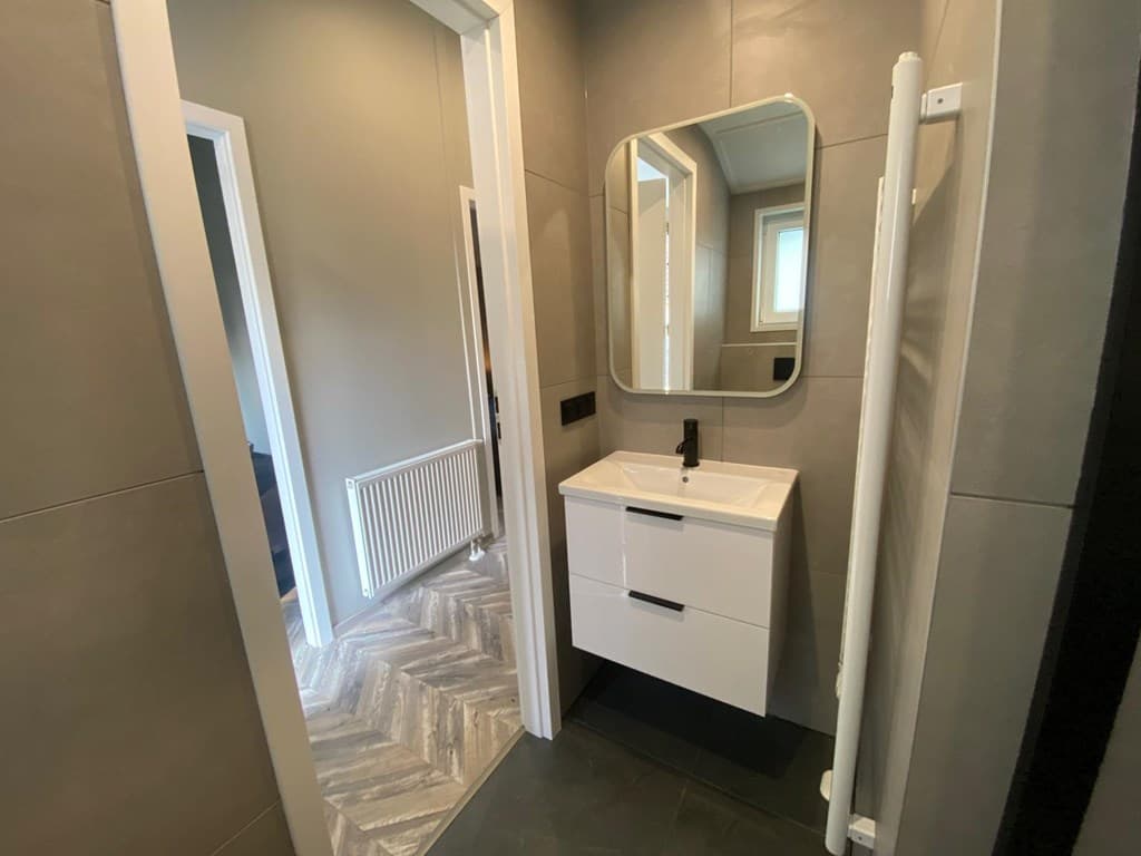 Moderne badkamer met wastafel, spiegel en handdoekradiator, naast een doorgang naar een andere ruimte.