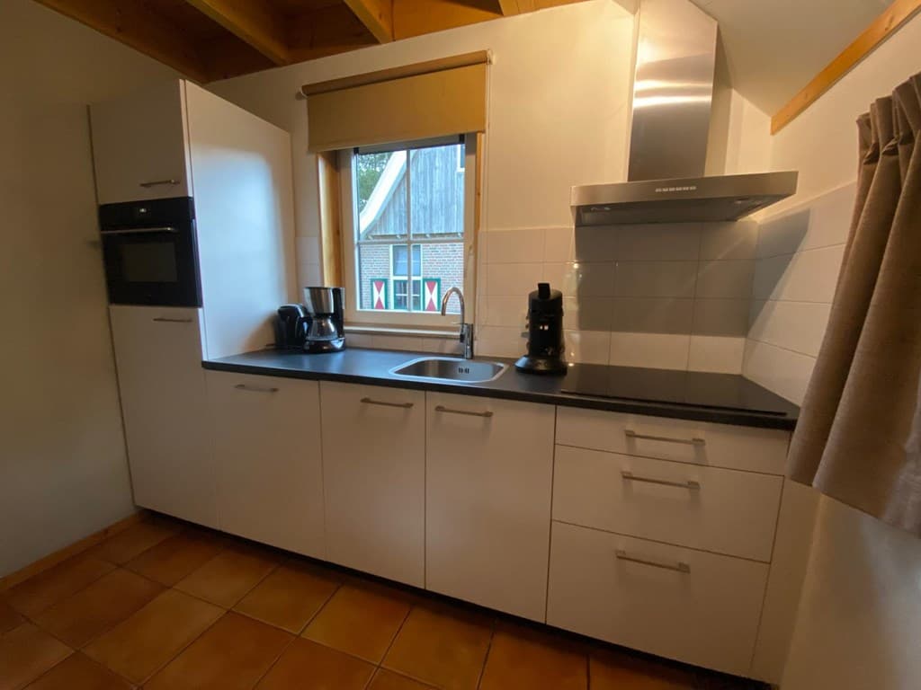 Keuken met moderne indeling, witte kasten, aanrecht met spoelbak en ramen die uitkijken op de buitenomgeving.