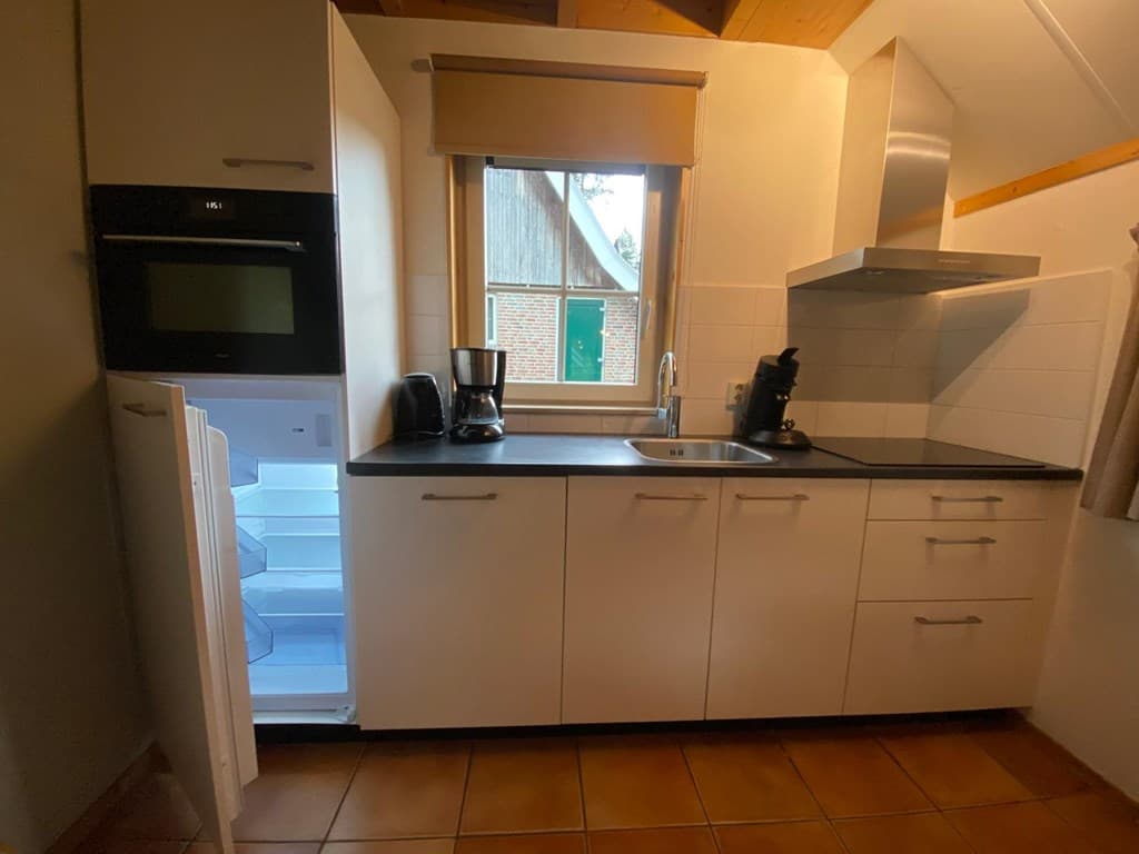 Moderne keuken met oven, koelkast, koffiezetapparaat en aanrecht, voorzien van lichtgekleurde kasten en tegelvloer
