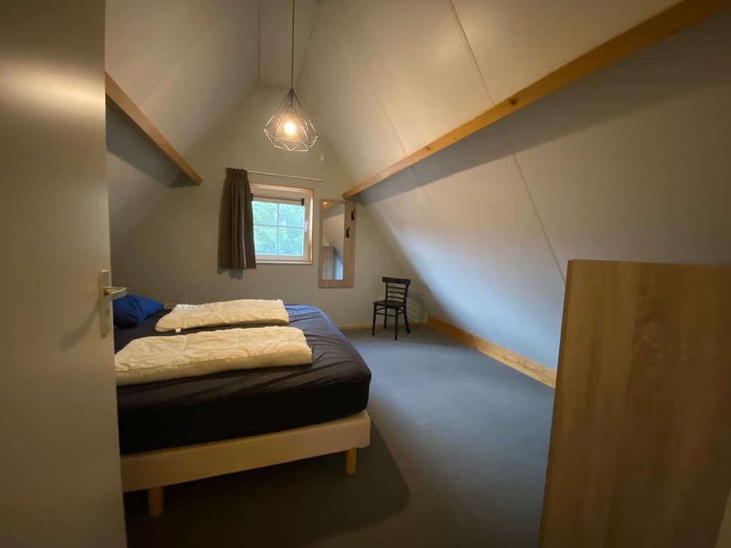 Slaapkamer met twee eenpersoonsbedden, een stoel en een raam met uitzicht naar buiten.