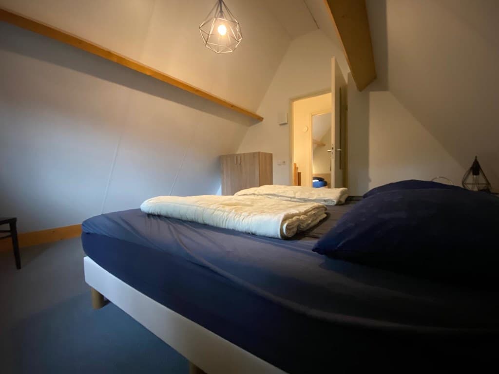 Slaapkamer met een tweepersoonsbed, houten vloer en sfeervolle verlichting aan het plafond.