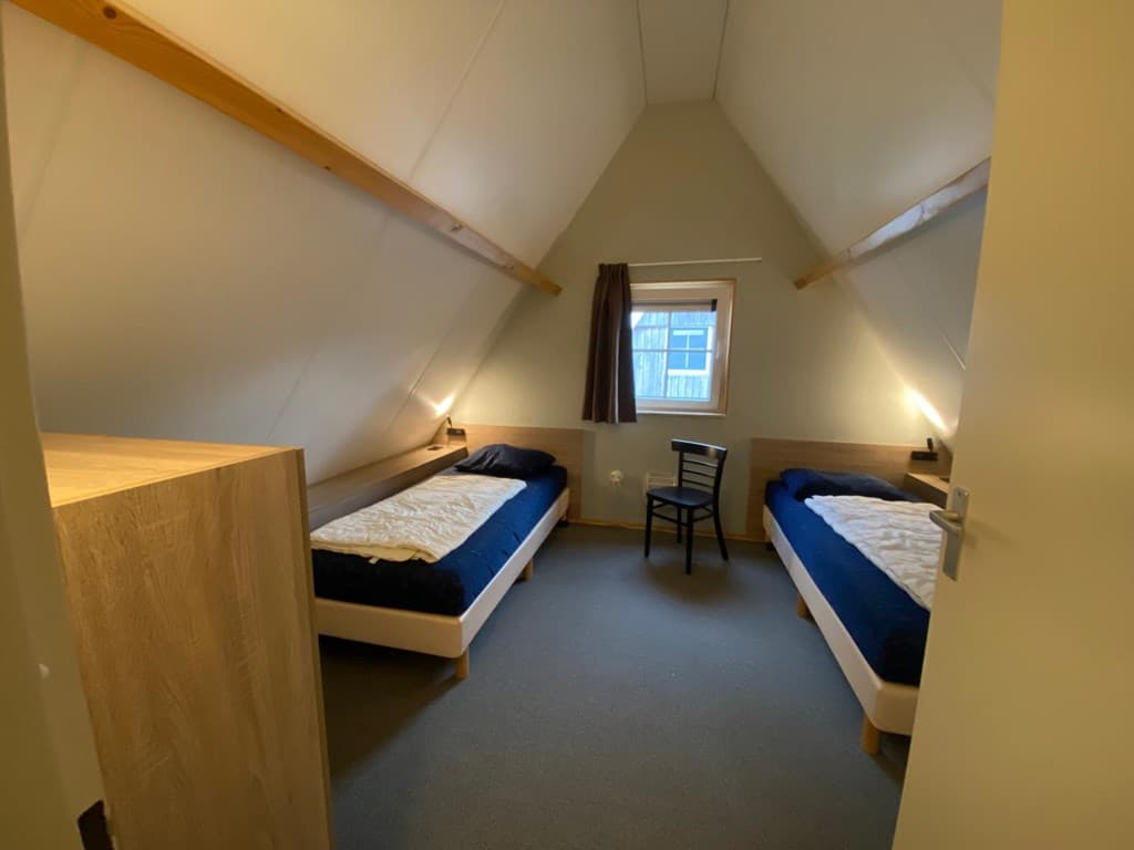 Slaapkamer met twee eenpersoonsbedden, een stoel en een kast onder een hellend dak.