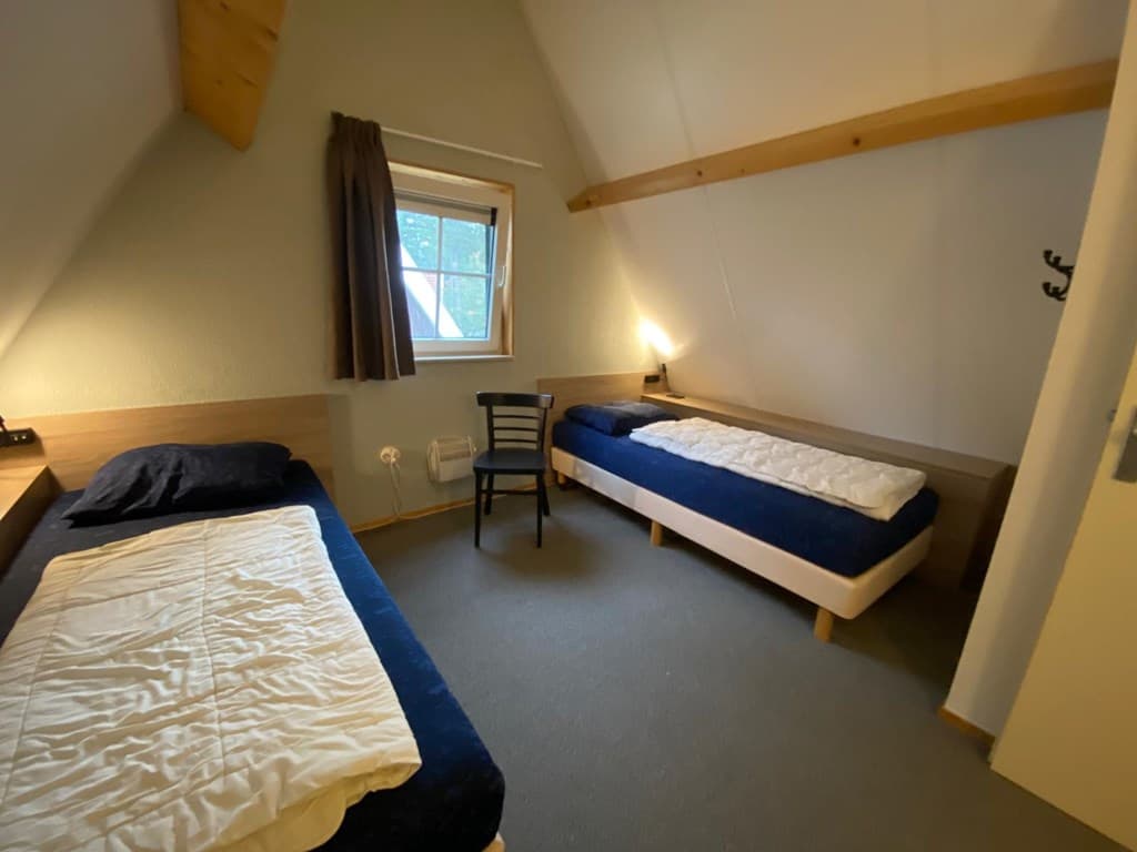 Slaapkamer met twee eenpersoonsbedden, een stoel en een raam met uitzicht op de natuur.