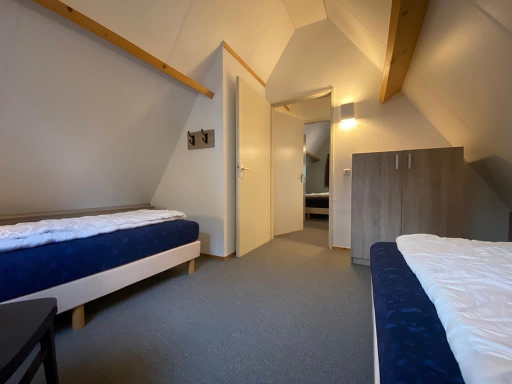 Slaapkamer met twee eenpersoonsbedden, een kledingkast en een deur naar een andere ruimte met schuin plafond.