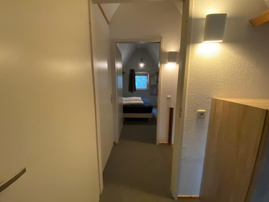 Overzicht van de gang met deuren naar een slaapkamer en een kast, lichte muren en vloerkleed aan de vloer