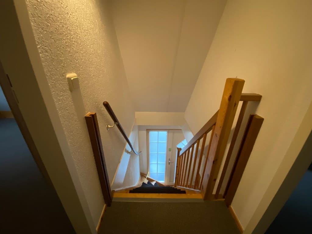 Trap met houten leuning die leidt naar een deur met glazen panelen aan de onderzijde van een woning.