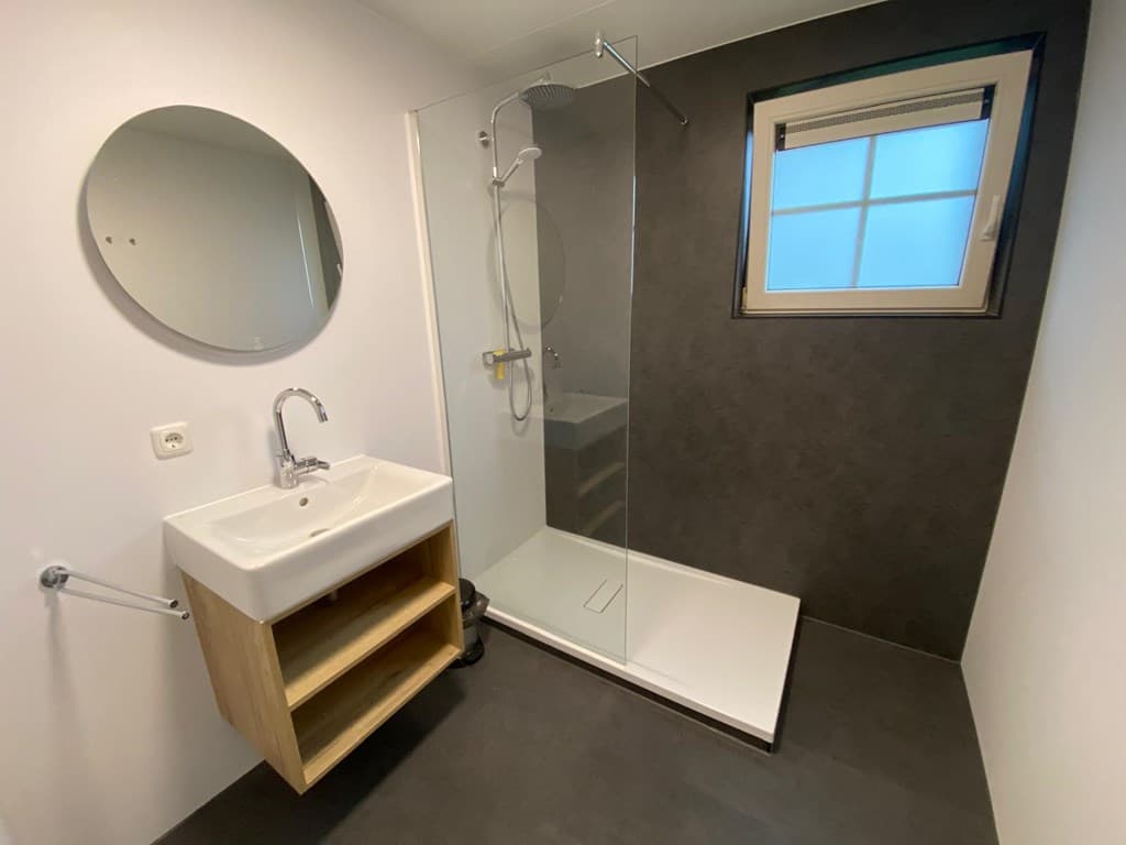 Moderne badkamer met douche, wastafel met onderkast en een raam met een ronde spiegel aan de muur