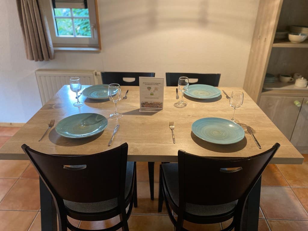 Eetkamer met een houten tafel, vier stoelen, gedekte tafel met glazen, borden en bestek.