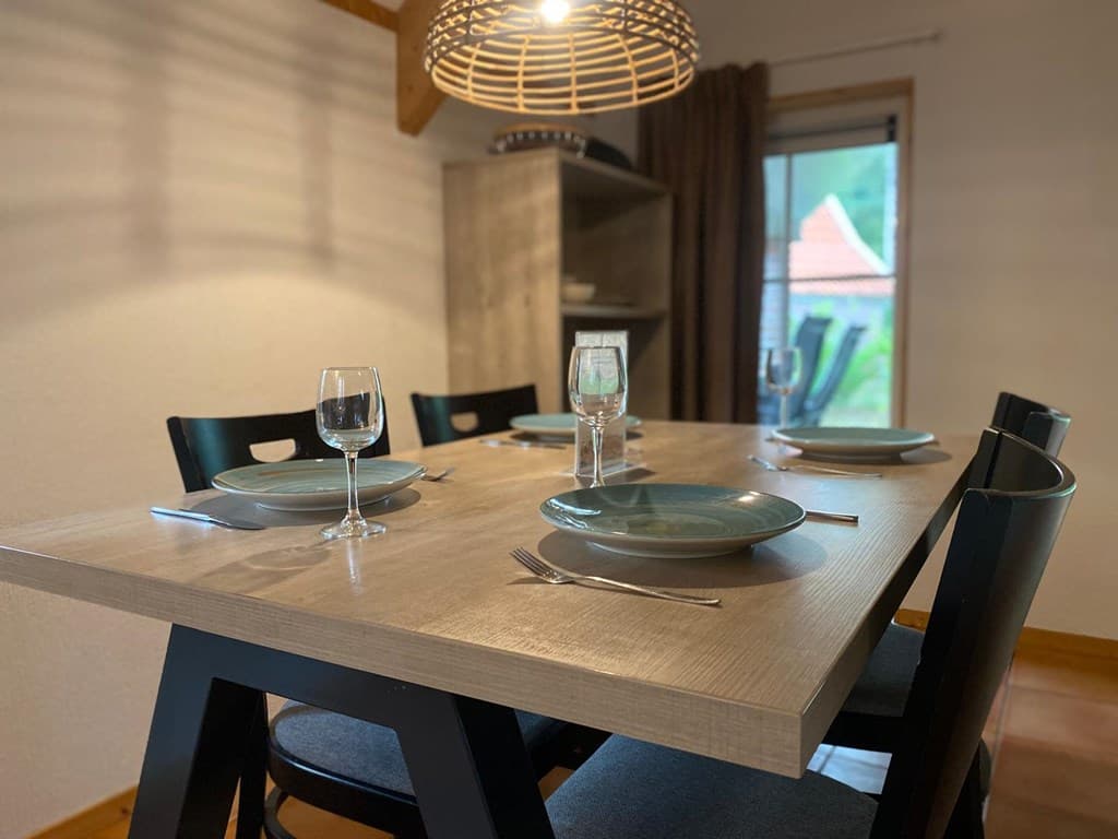 Eetkamertafel met zes stoelen, borden en glazen, met uitzicht naar buiten door een raam.