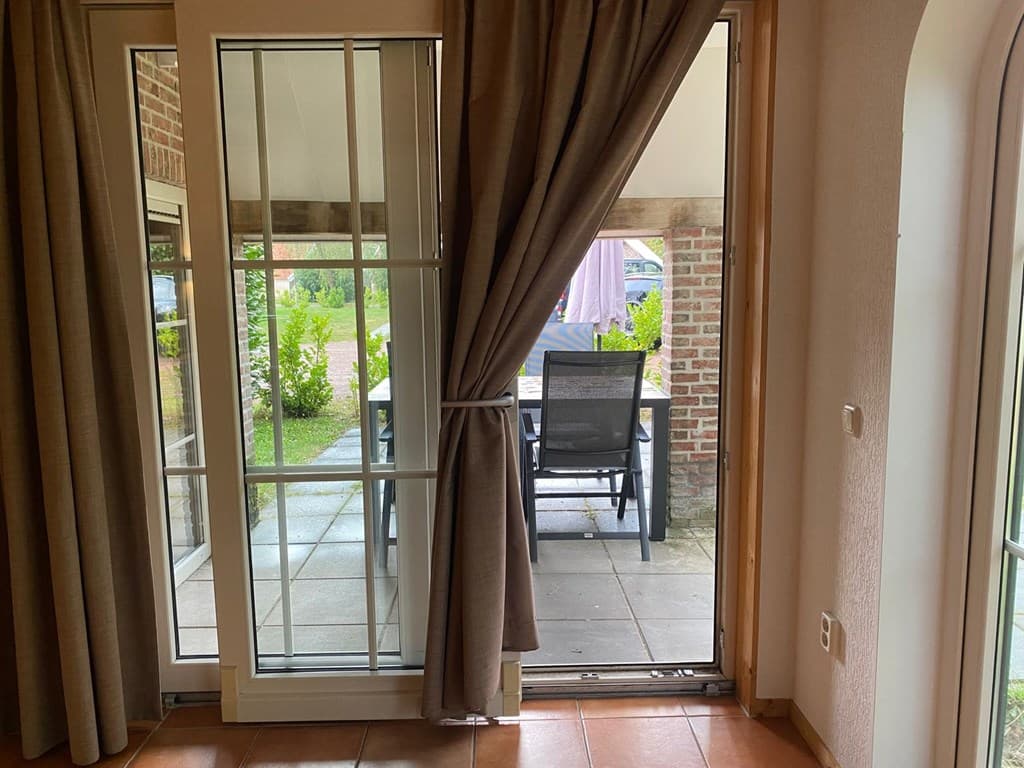 Uitzicht vanuit de woning op een betegeld terras met een tuintafel en stoelen, omringd door groen.