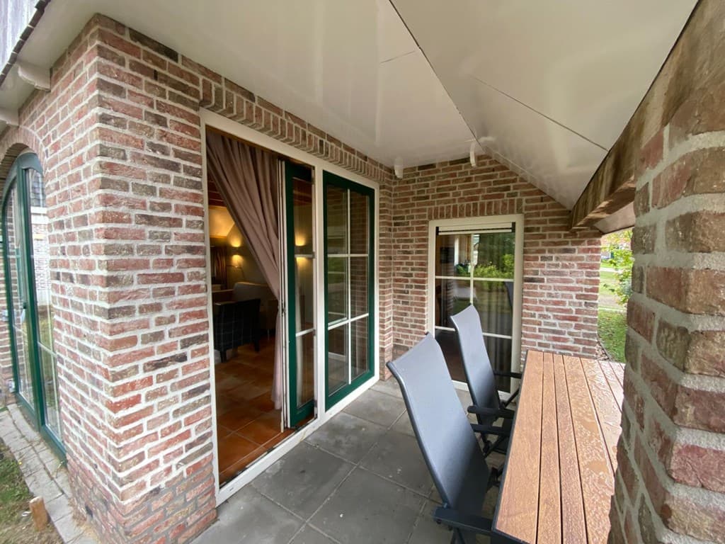 Buitenterras met een tafeltje en stoelen, zicht op de ingang van de woning met bakstenen muren en grote ramen