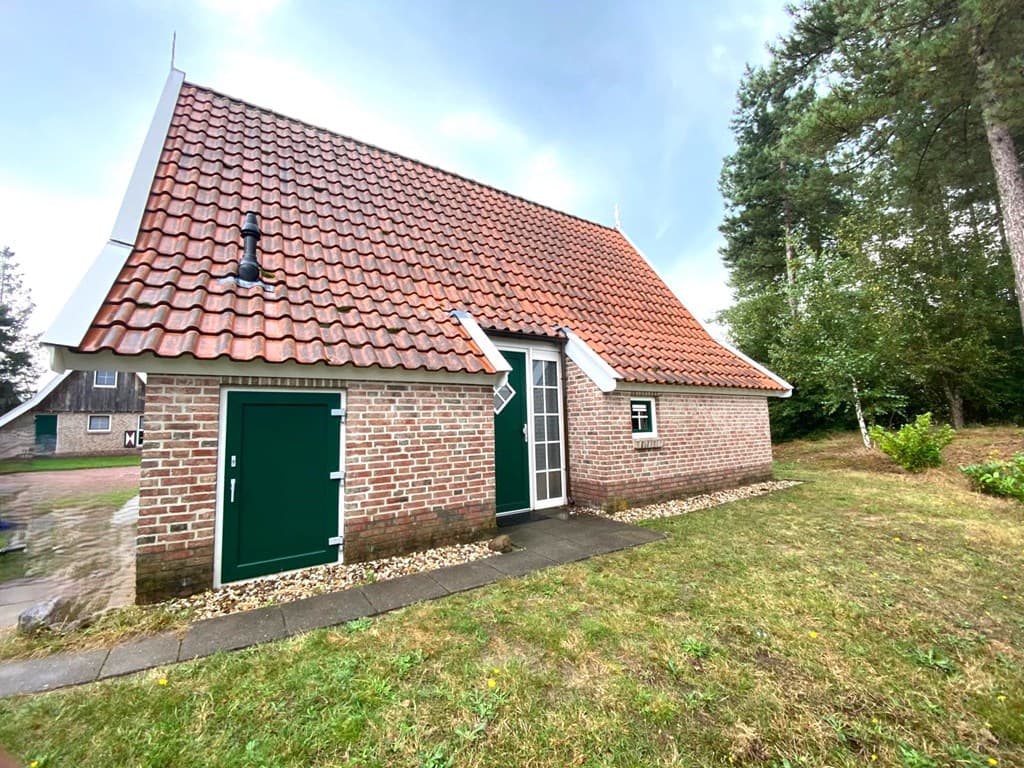 Vakantiehuis met een rode schuine dakbedekking en een groene deur, omgeven door een grasveld en bomen.