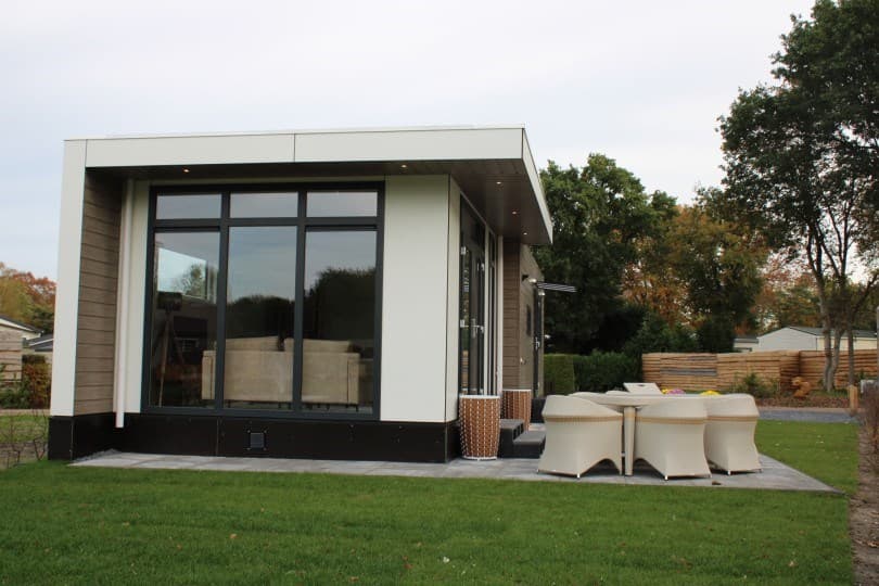 Moderne vakantiewoning met grote ramen en terras, omgeven door groen gras en bomen op Camping De Konijnenberg.