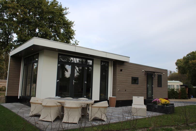Moderne vakantiewoning met grote glazen deuren, terras en vier witte stoelen met tafeltje aan de voorkant.