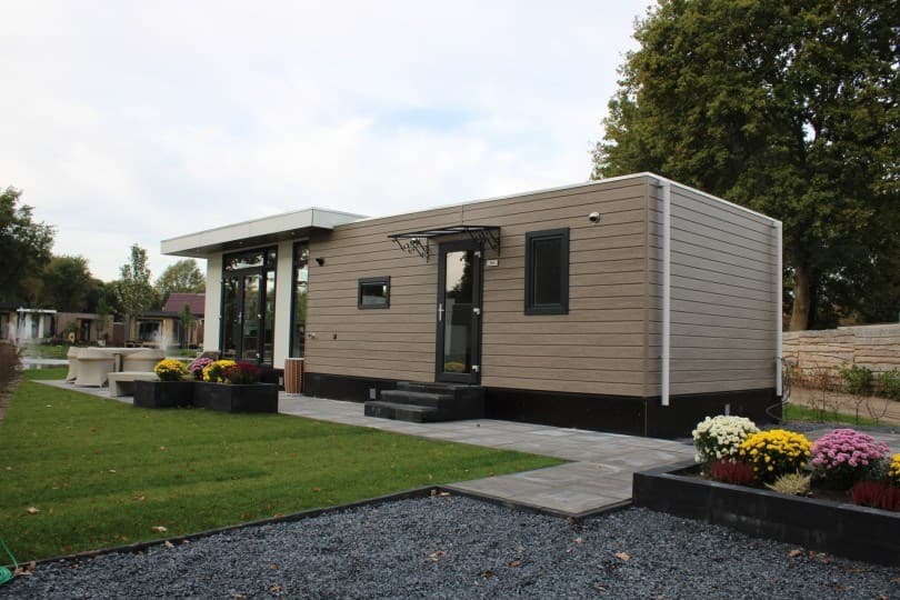 Moderne bungalow met een stenen terras, tuin met gras en bloembakken aan de voorkant, gelegen op Camping De Konijnenberg.